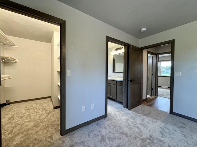 unfurnished bedroom with ensuite bathroom, sink, light colored carpet, and a spacious closet