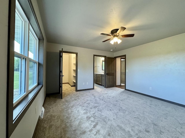 unfurnished bedroom with ceiling fan, light colored carpet, ensuite bathroom, and a walk in closet