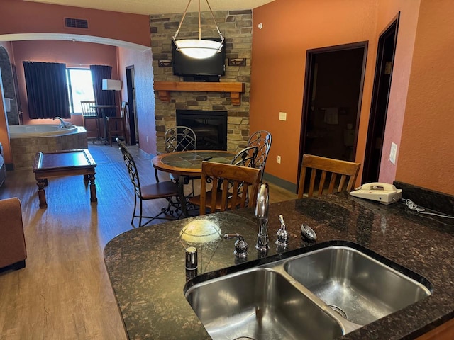 kitchen featuring pendant lighting, a fireplace, hardwood / wood-style floors, sink, and dark stone counters