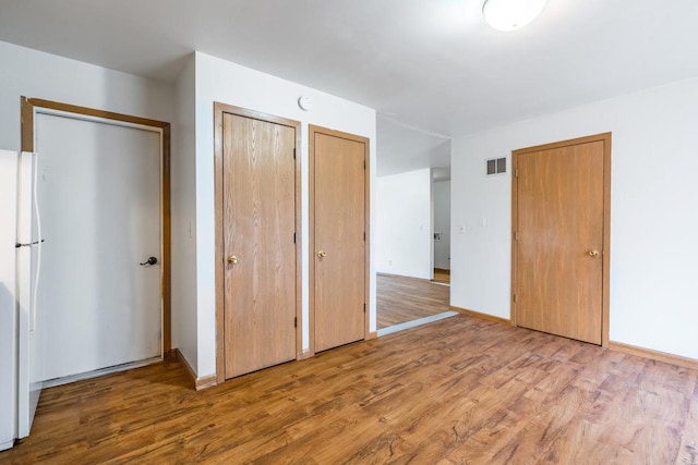 unfurnished bedroom featuring white refrigerator, hardwood / wood-style floors, and two closets