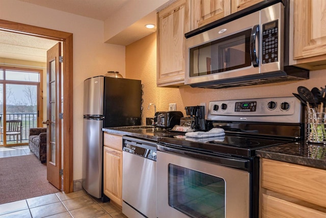 kitchen with appliances with stainless steel finishes, light brown cabinets, sink, light tile flooring, and dark stone countertops