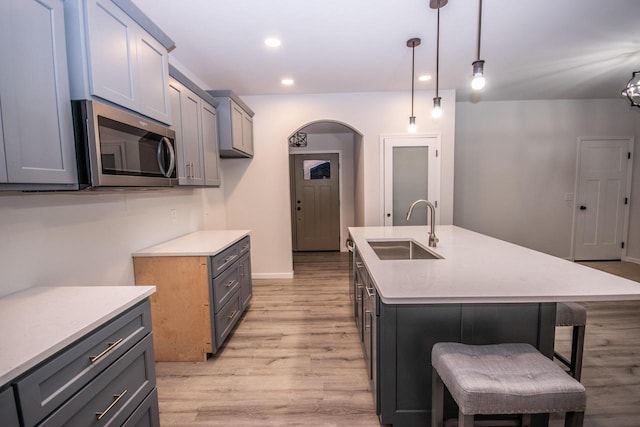 kitchen with a kitchen breakfast bar, a kitchen island with sink, sink, decorative light fixtures, and light hardwood / wood-style floors