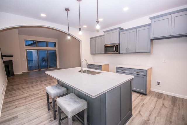 kitchen featuring sink, pendant lighting, light hardwood / wood-style floors, gray cabinets, and a center island with sink