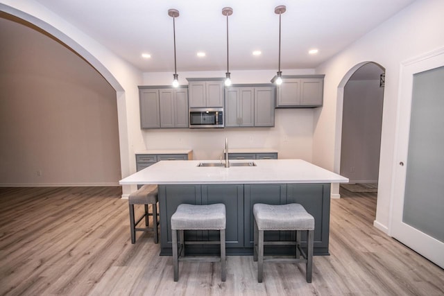 kitchen with decorative light fixtures, light wood-type flooring, a center island with sink, and sink