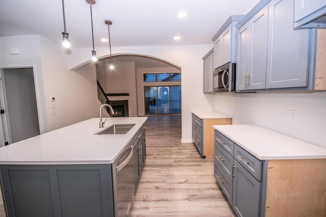 kitchen featuring a center island with sink, sink, hanging light fixtures, light wood-type flooring, and stainless steel appliances