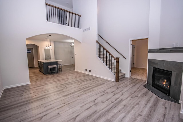 unfurnished living room featuring a tile fireplace, a high ceiling, light wood-type flooring, and sink