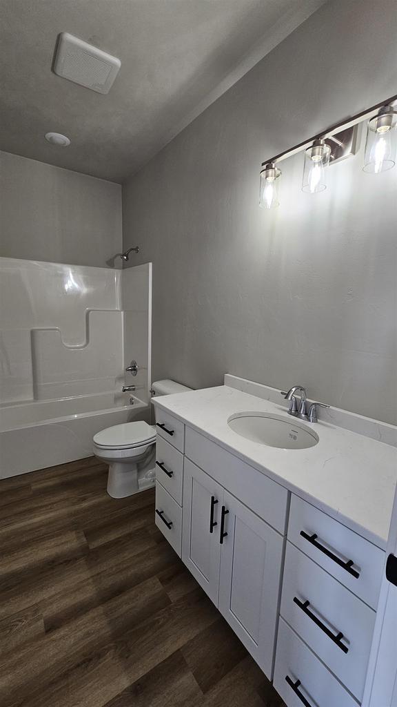 full bathroom featuring washtub / shower combination, wood-type flooring, vanity, and toilet