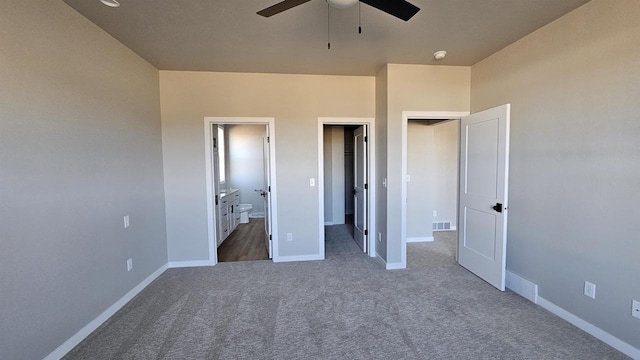 unfurnished bedroom featuring connected bathroom, dark carpet, and ceiling fan