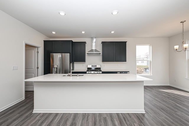 kitchen featuring range, sink, wall chimney range hood, stainless steel fridge, and a center island with sink