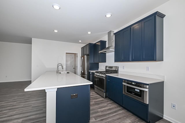 kitchen with appliances with stainless steel finishes, sink, wall chimney range hood, blue cabinetry, and dark hardwood / wood-style flooring