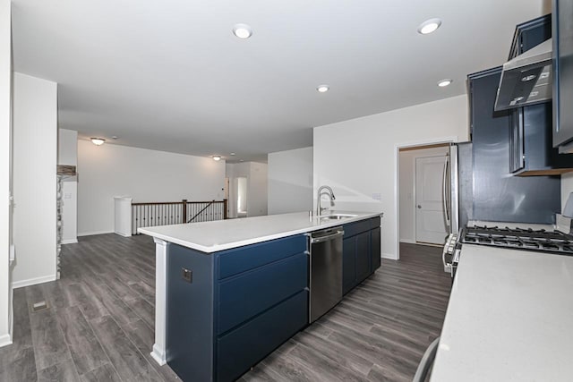 kitchen with wall chimney exhaust hood, dark wood-type flooring, blue cabinetry, sink, and dishwasher