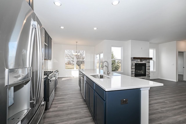 kitchen featuring a stone fireplace, appliances with stainless steel finishes, dark wood-type flooring, and sink