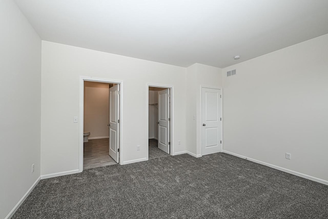 unfurnished bedroom with connected bathroom, a walk in closet, a closet, and dark colored carpet