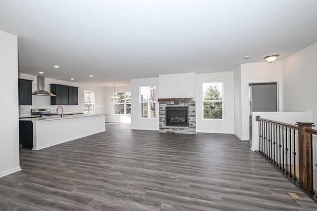 unfurnished living room with a healthy amount of sunlight, dark wood-type flooring, a notable chandelier, and a stone fireplace