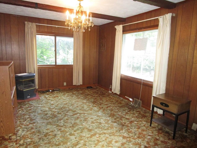 carpeted empty room featuring beam ceiling, a chandelier, and wooden walls