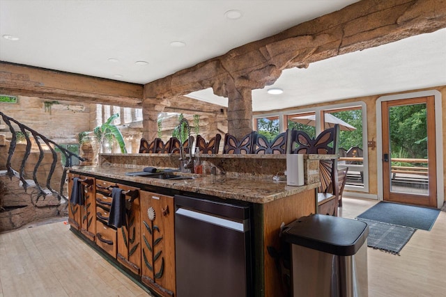 kitchen with light hardwood / wood-style flooring, dark stone counters, a kitchen island with sink, sink, and stainless steel dishwasher