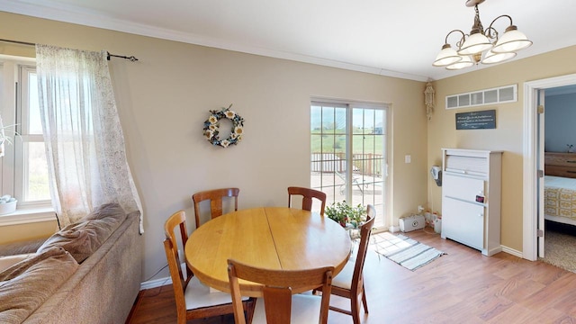 dining area with wood-type flooring, an inviting chandelier, and ornamental molding