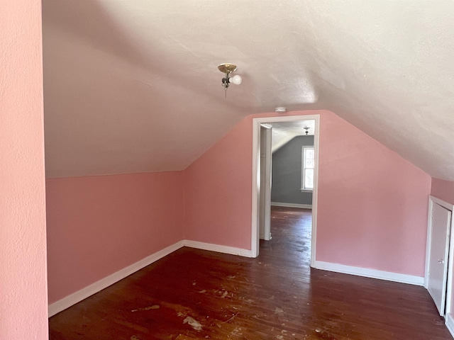 additional living space with dark wood-style floors, baseboards, and vaulted ceiling