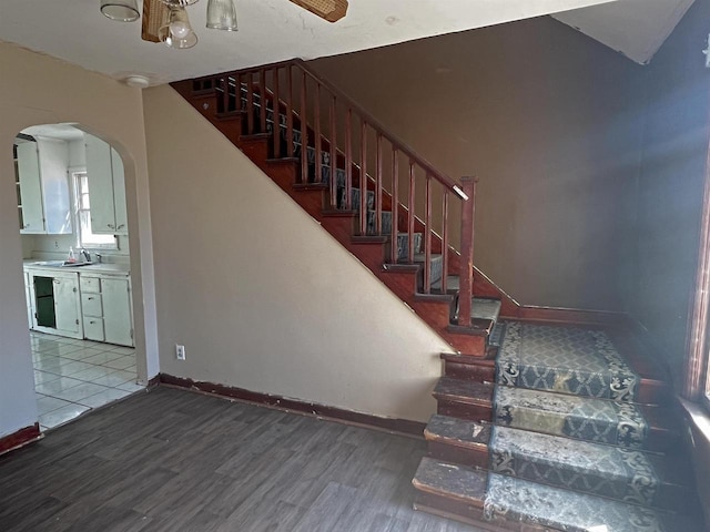 stairway featuring arched walkways, baseboards, and wood finished floors