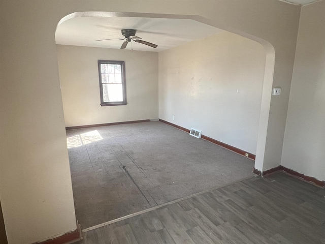 empty room featuring dark wood-style floors, arched walkways, visible vents, ceiling fan, and baseboards