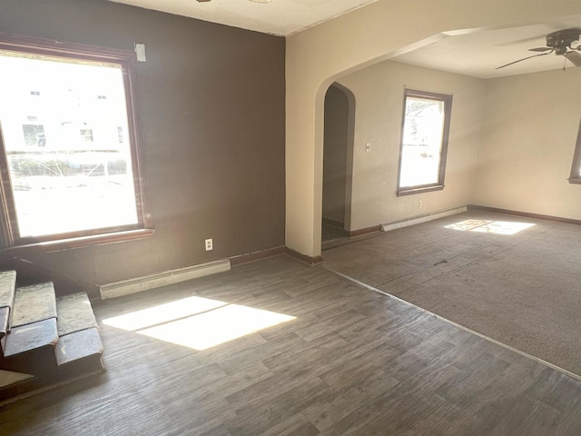 spare room featuring a baseboard heating unit, wood finished floors, arched walkways, and a ceiling fan