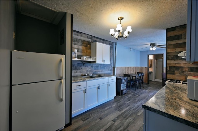 kitchen with ceiling fan with notable chandelier, white refrigerator, wood walls, and sink