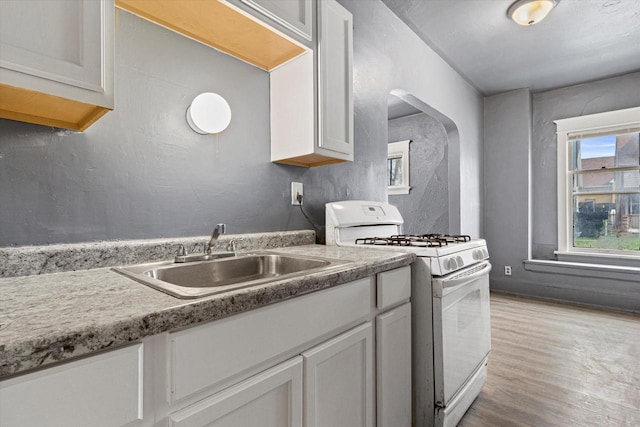 kitchen with white cabinetry, light wood-type flooring, sink, and gas range gas stove