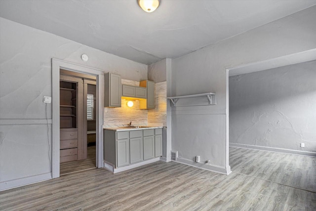 kitchen featuring light wood-type flooring, tasteful backsplash, gray cabinetry, and sink