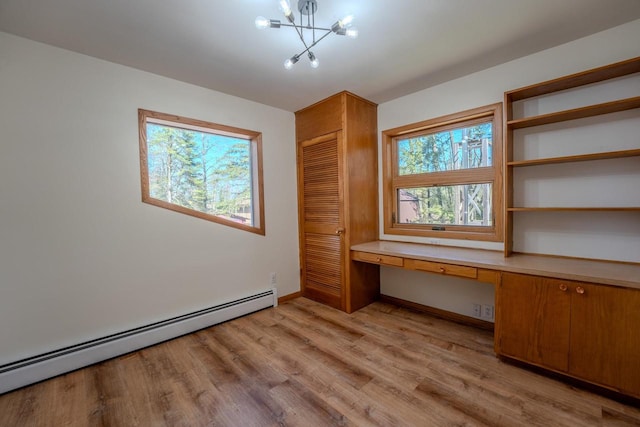 unfurnished office featuring light hardwood / wood-style flooring, built in desk, a baseboard radiator, and a notable chandelier