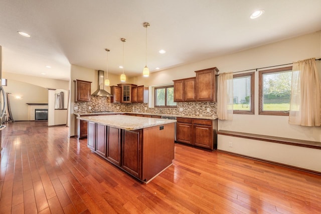 kitchen with a center island, hanging light fixtures, wall chimney range hood, hardwood / wood-style flooring, and tasteful backsplash