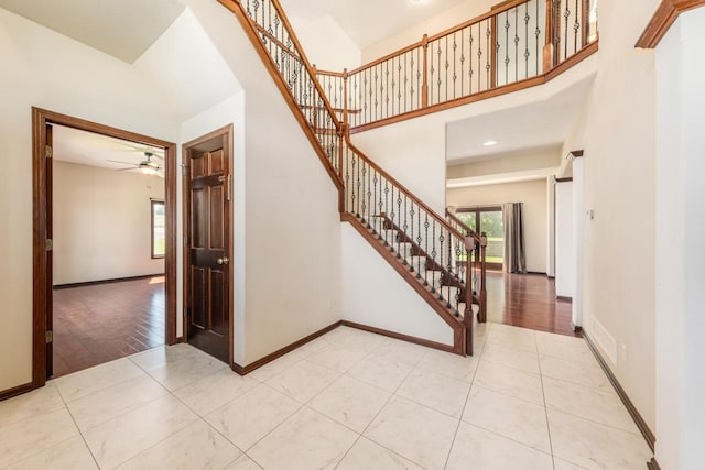 stairway with a high ceiling, ceiling fan, and light tile floors