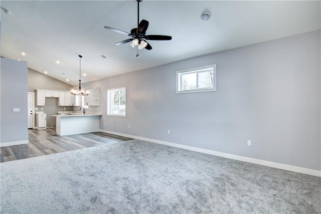 unfurnished living room featuring light colored carpet, lofted ceiling, and ceiling fan with notable chandelier