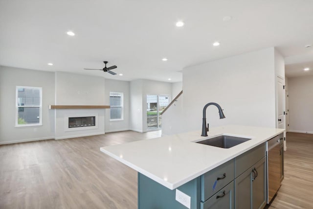 kitchen featuring a kitchen island with sink, sink, stainless steel dishwasher, and light hardwood / wood-style flooring