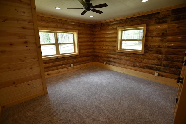 empty room with ceiling fan, log walls, and dark carpet