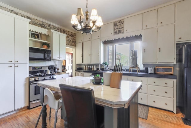 kitchen with decorative light fixtures, black appliances, light wood-type flooring, a center island, and white cabinetry