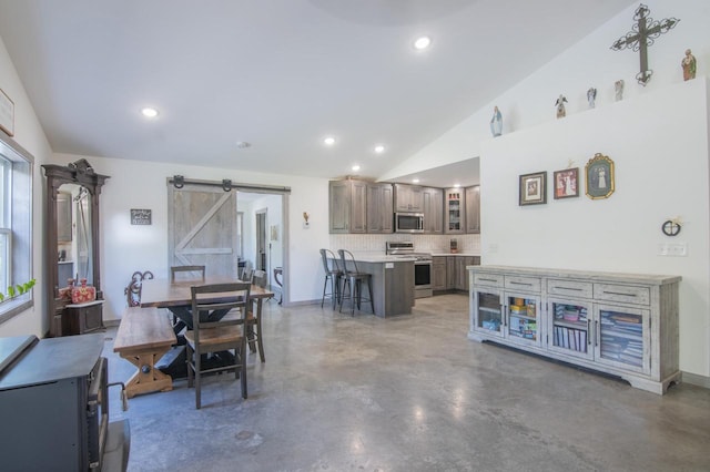 dining area with a barn door, concrete flooring, and vaulted ceiling