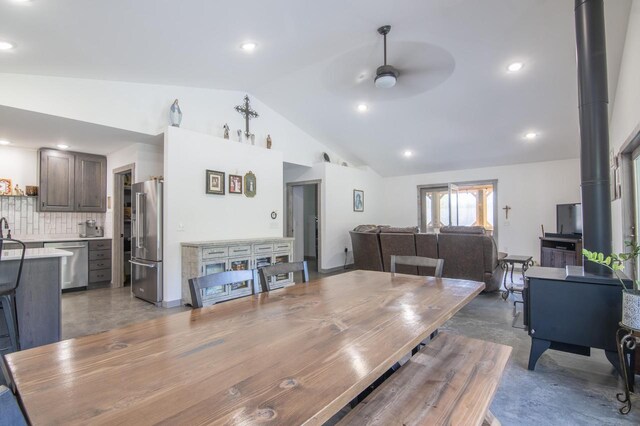 dining area with ceiling fan, concrete floors, a wood stove, high vaulted ceiling, and sink