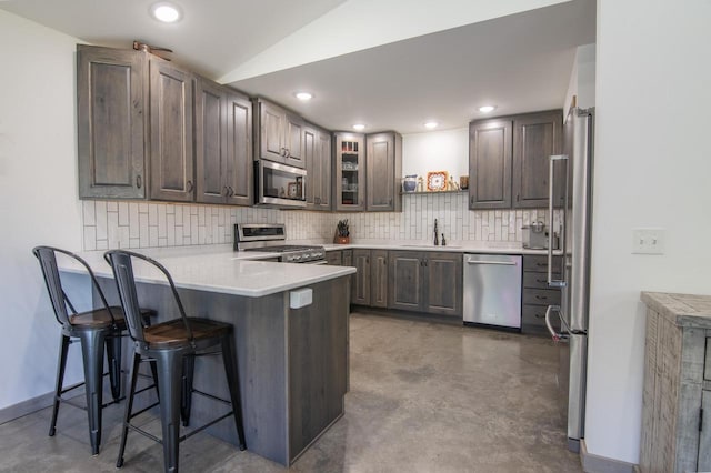 kitchen featuring a kitchen breakfast bar, concrete floors, backsplash, and appliances with stainless steel finishes