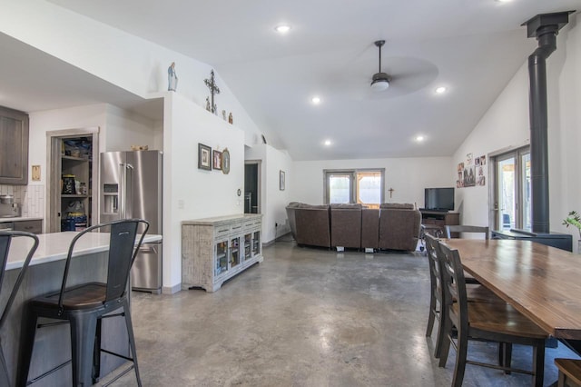 dining space featuring concrete flooring, ceiling fan, vaulted ceiling, and a wood stove