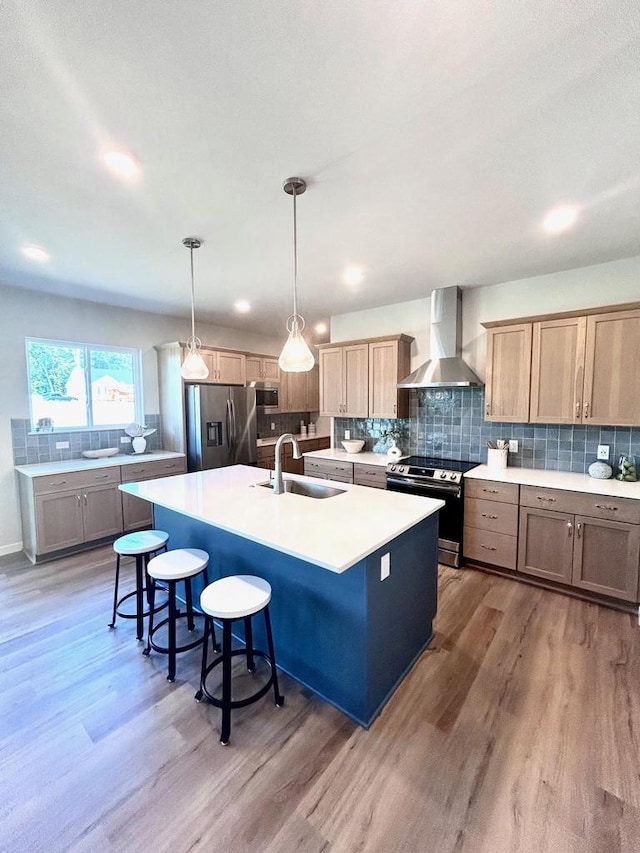 kitchen featuring sink, hardwood / wood-style flooring, appliances with stainless steel finishes, a center island with sink, and wall chimney exhaust hood