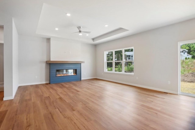 unfurnished living room with a raised ceiling, ceiling fan, and light wood-type flooring