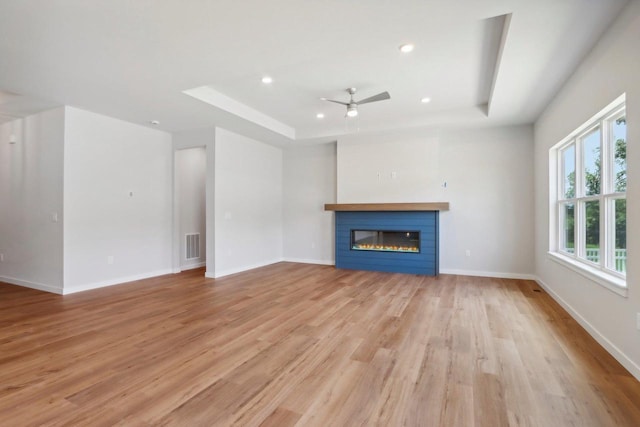 unfurnished living room featuring ceiling fan, light hardwood / wood-style floors, and a tray ceiling