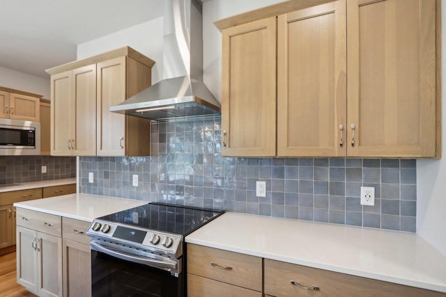 kitchen featuring light brown cabinetry, decorative backsplash, wall chimney exhaust hood, and appliances with stainless steel finishes