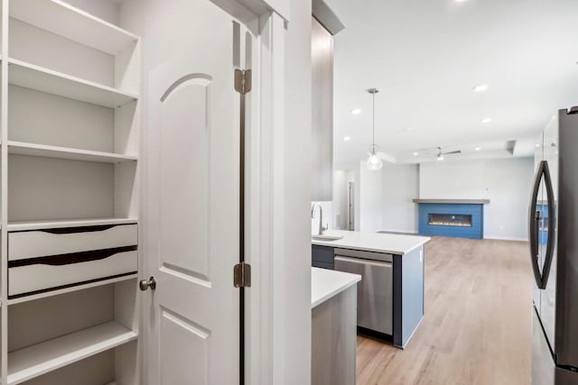 kitchen featuring stainless steel appliances, hanging light fixtures, sink, and light wood-type flooring