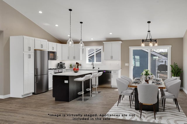 kitchen featuring a center island, white cabinetry, appliances with stainless steel finishes, hardwood / wood-style floors, and decorative light fixtures