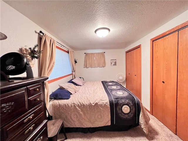 bedroom with two closets, a textured ceiling, and carpet flooring