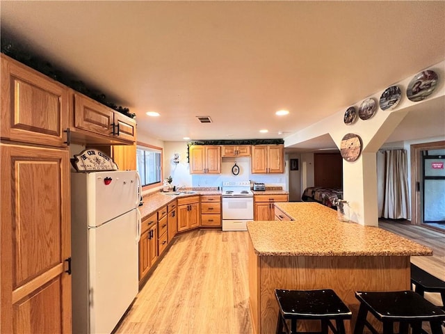 kitchen featuring a kitchen breakfast bar, light hardwood / wood-style flooring, kitchen peninsula, white appliances, and sink