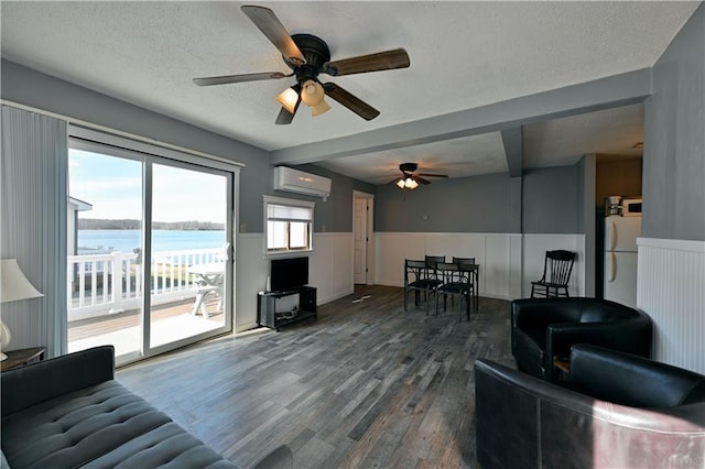 living room featuring dark hardwood / wood-style floors, ceiling fan, a water view, a wall mounted air conditioner, and a textured ceiling