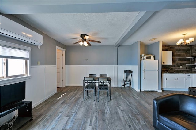 unfurnished dining area with a wall mounted air conditioner, ceiling fan with notable chandelier, a textured ceiling, and dark wood-type flooring