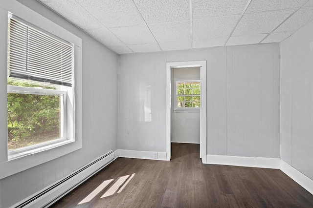 unfurnished room featuring a baseboard heating unit, dark hardwood / wood-style floors, and a paneled ceiling